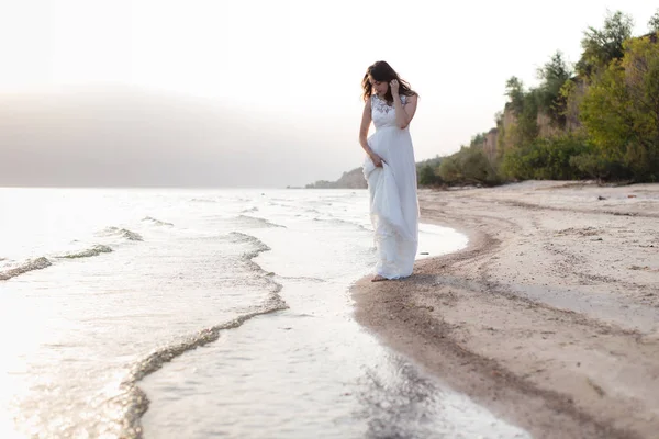 Vacker ung brunett kvinna i vit lång klänning vid havet — Stockfoto
