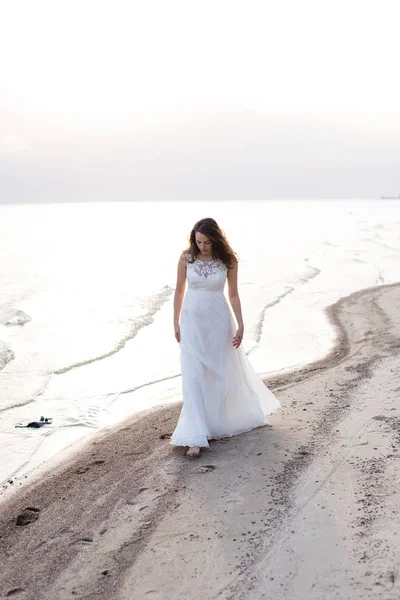 Mulher morena jovem bonita em vestido longo branco na costa do mar — Fotografia de Stock