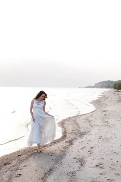 Vacker ung brunett kvinna i vit lång klänning vid havet — Stockfoto