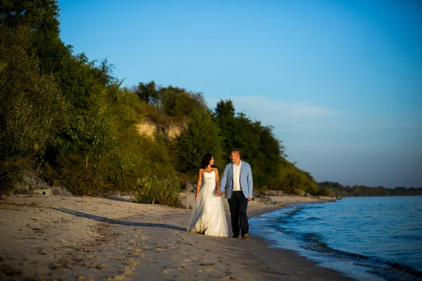 Retrato de casal de amantes recém-casados na natureza. Brunette noiva em vestido de noiva com um belo penteado, véu e maquiagem e seu marido em um terno — Fotografia de Stock