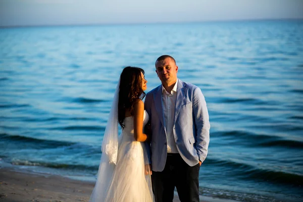 Retrato de casal de amantes recém-casados na natureza. Brunette noiva em vestido de noiva com um belo penteado, véu e maquiagem e seu marido em um terno — Fotografia de Stock