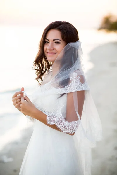 Retrato de noiva morena em vestido de noiva com um belo penteado, véu e maquiagem à beira-mar — Fotografia de Stock