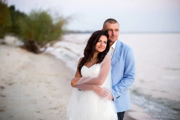 Retrato de casal de amantes recém-casados na natureza. Brunette noiva em vestido de noiva com um belo penteado, véu e maquiagem e seu marido em um terno — Fotografia de Stock