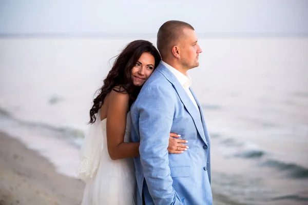 Retrato de pareja de amantes recién casados sobre la naturaleza. Morena novia en vestido de novia con un hermoso peinado, velo y maquillaje y su marido en un traje —  Fotos de Stock