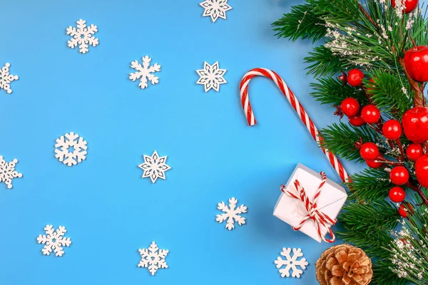 Noel arkaplanı. Hediye kutusu. Firavun dalı ve konisi. Kırmızı çilek. Kar taneleri. Lolipop. Mavi arka plan. Üst Manzara. Yakın plan..