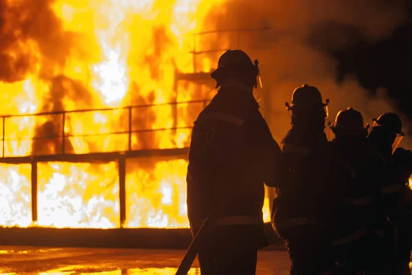 Raden av brandmän står med slang framför brinnande struktur under brandbekämpning träning — Stockfoto