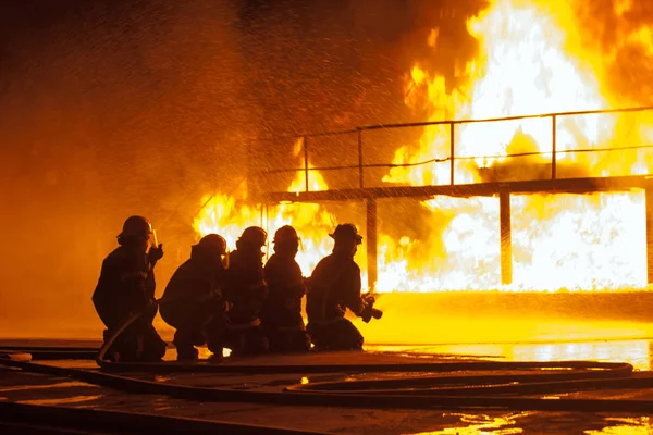 Group of firefighters spraying down burning structure during firefighting exercise — Stock Photo, Image