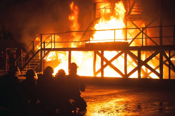 Группа пожарных на коленях перед горящим зданием во время учений по пожаротушению — стоковое фото
