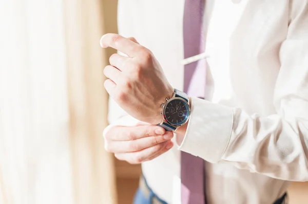 A man in a white shirt adjusts his watch