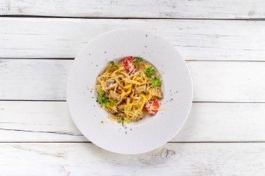 Beyaz ahşap arka planda kremalı soslu tavuk ve mantarlı makarna. Üst görünüm