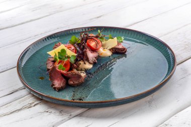 Peynirli sulu biftek, beyaz ahşap arka planda ton balığı soslu domates.