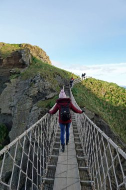 Turist kız, Kuzey İrlanda 'nın popüler turistik merkezi Carrick-a-rede Rope Köprüsü' nü geçiyor. Ballintoy, County Antrim, Kuzey İrlanda 18.11.2019