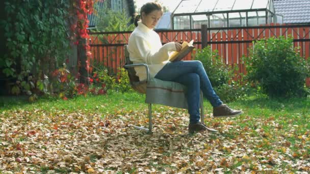Beautiful young woman reading book in backyard — Stock Video