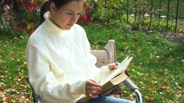 Mujer en jersey blanco lee un libro al aire libre — Vídeos de Stock