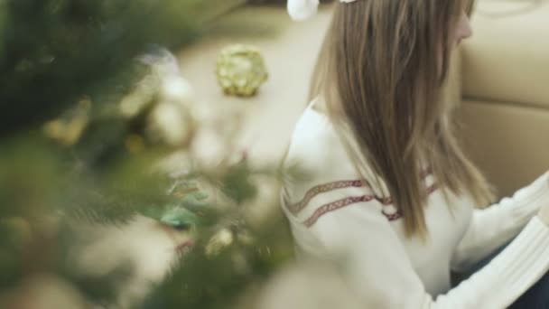 Pretty girl in christmas cap using smartphone behind christmas tree — Stock Video