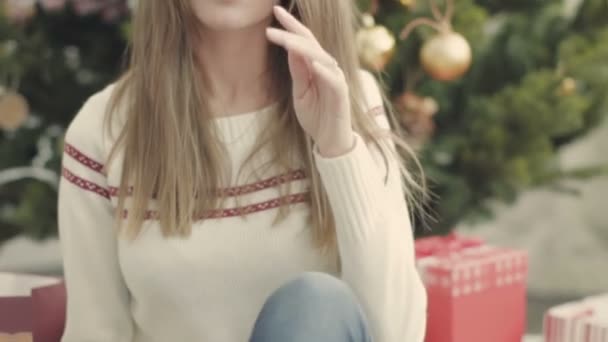꾸며진된 크리스마스 나무에 앉아 흰 니트 스웨터에 귀여운 여자 — 비디오