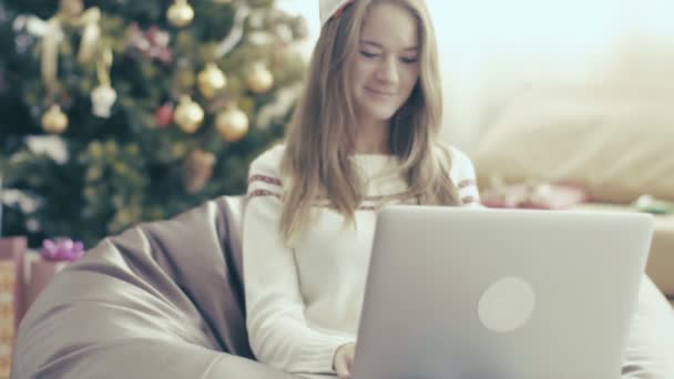 Leende flicka i jul locket med laptop på mjuk stol — Stockvideo