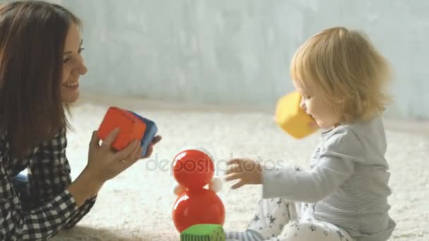 Moeder en haar dochtertje speelt met kubussen en pop op tapijt — Stockvideo