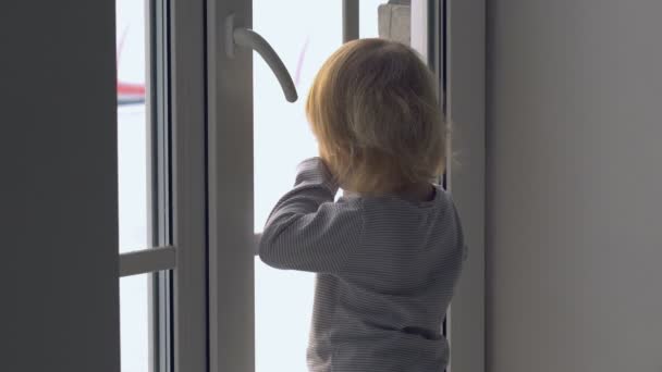 Kis baba lány állt, az ablak mellett, és látszó kívül — Stock videók
