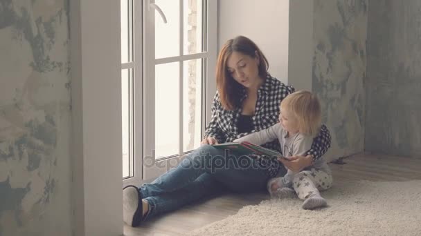Pencere ve bir kitap okuma yakınındaki küçük kızı sandalyeyle anne — Stok video