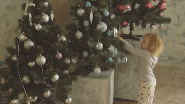 Pouco bonito menina pontos com dedo bolas de Natal na árvore decorada — Vídeo de Stock