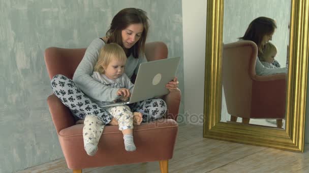 Красивая женщина использует ноутбук с маленьким ребенком на коленях — стоковое видео