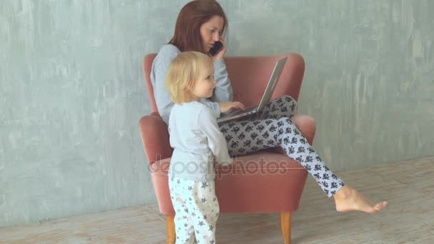 Молодая женщина отталкивает свою маленькую дочь, разговаривая на смартфоне — стоковое видео