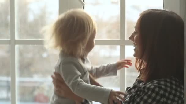 Mother plays with daughter against window — Stock Video