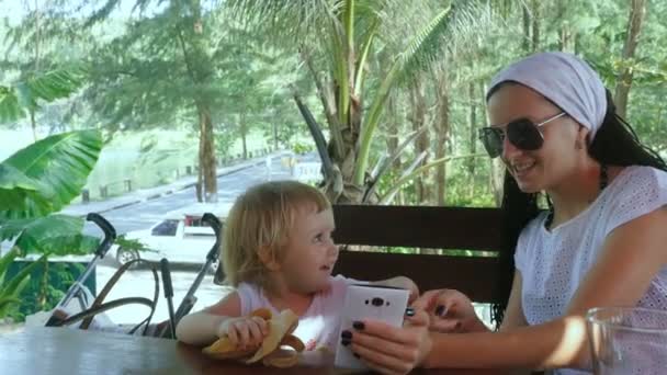 Mãe com filha sentada no café e usando smartphone — Vídeo de Stock