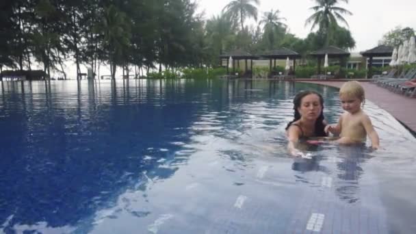 Young woman with daughter smells flower plumeria in pool — Stockvideo