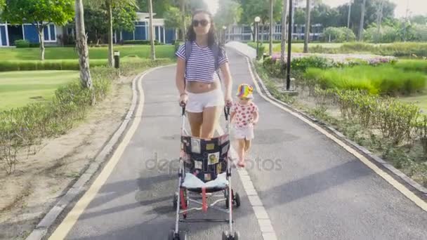 Жінка в сонцезахисних окулярах йде з дитиною і коляскою — стокове відео