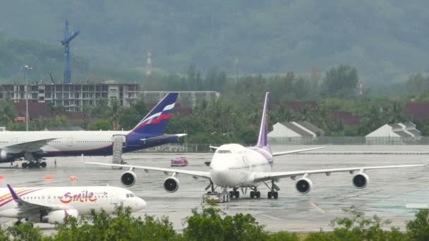 Taxi aerei sul campo d'aviazione contro il Boeing 747 in piedi con macchina trainatrice sul carrello di atterraggio — Video Stock