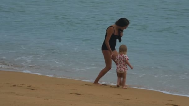 Mother and daughter are running on the beach from ocean waves — Stock Video