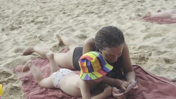 Mãe brinca com filhinha usando smartphone na praia — Vídeo de Stock
