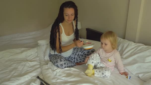 Tablet bilgisayarda bakarken küçük bebek kız yulaf lapası besleme güzel genç kadın — Stok video