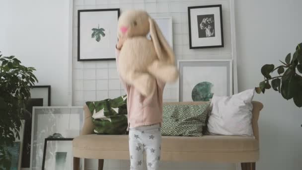 小さな女の子がぬいぐるみのウサギをスローします。 — ストック動画