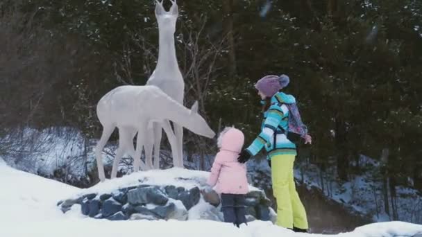 Young woman with daughter stay near statue of a deer — Stock Video