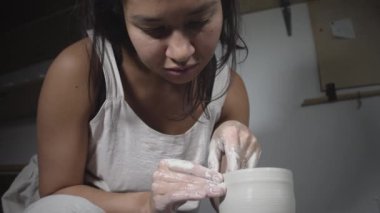 Asyalı kadın çömlekçi atölyede çömlekçi çarkında kil kalıbı yapıyor.