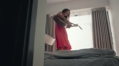 Güzel kız gitarla yatakta dans ediyor.
