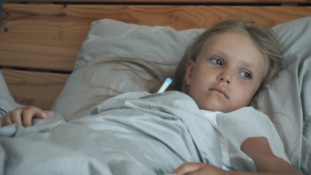 En liten sjuk flicka med termometer i sängen — Stockvideo