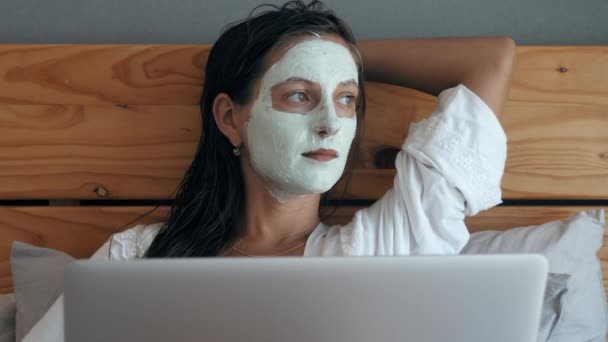 Mulher com máscara facial deitada na cama com laptop — Vídeo de Stock