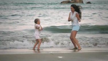 Anne ve kızı sahilde dans ediyor.