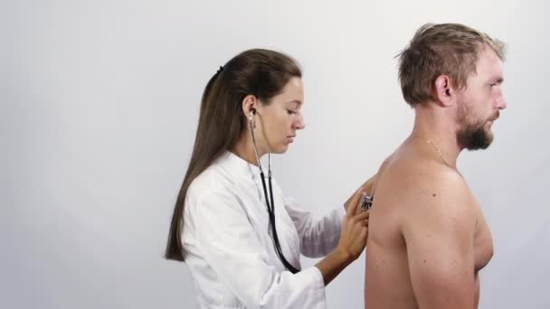 Женщина-врач осматривает пациента-мужчину при помощи стетоскопа — стоковое видео