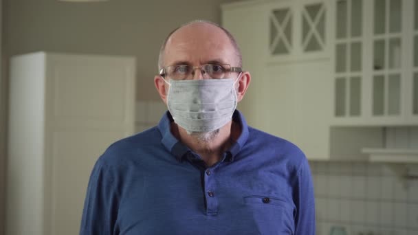 Старший чоловік в медичній масці і дивиться на камеру — стокове відео