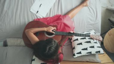 Kadın yatakta akustik gitar çalıyor.