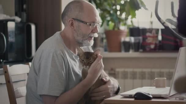 Старий працює на ноутбуці, що тримає домашню тварину — стокове відео