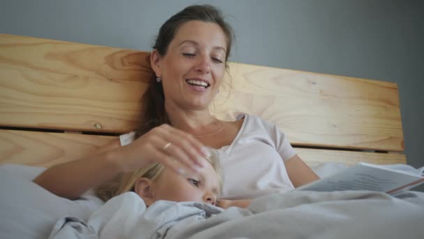 母亲和女儿躺在床上看书 — 图库视频影像