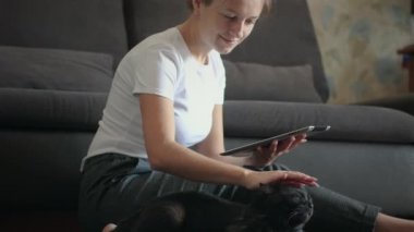 Tablet bilgisayar kullanan bir kadın kedisini okşuyor.