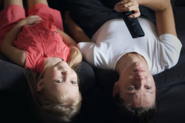 Sıkılmış anne-kız kanepede baş aşağı uzanmış televizyon izliyorlar.