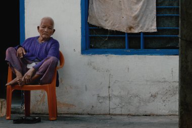 NHA TRANG, VIETNAM - JANUARY 21, 2020: Authentic Vietnamese old man sitting on a chair in the street and looking on people passing by